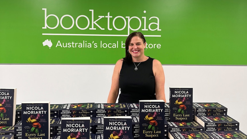 Nicola Moriarty standing in front of a green Booktopia sign, hundreds of copies of Every Last Suspect in front of her
