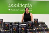 Nicola Moriarty standing in front of a green Booktopia sign, hundreds of copies of Every Last Suspect in front of her