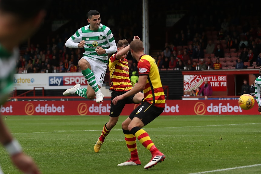 Celtic player Tom Rogic is seen mid-air after taking a shot as the ball flies toward the net.