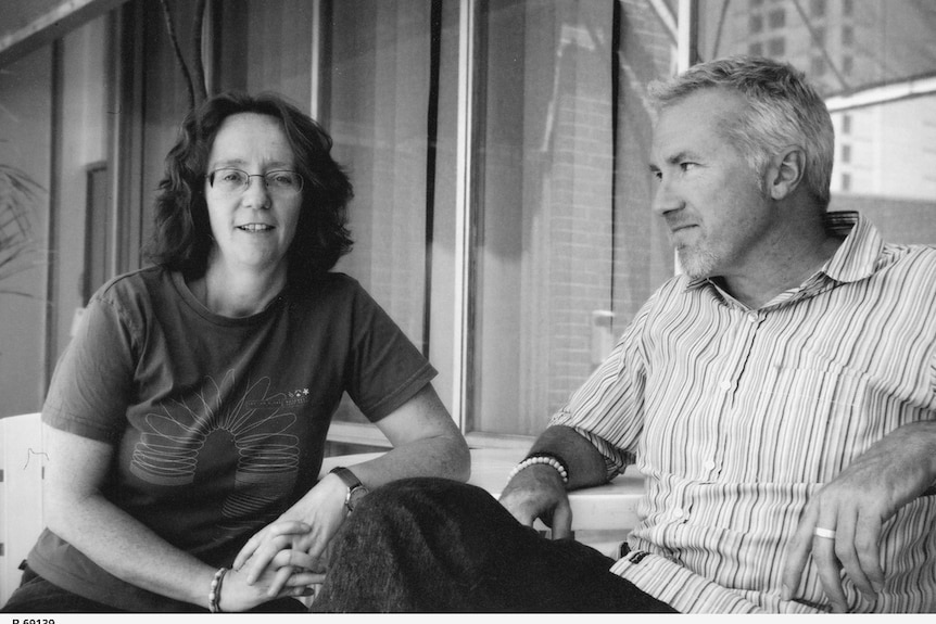 A woman wearing a dark shirt and a man wearing stripes sit on a balcony in a black and white photo