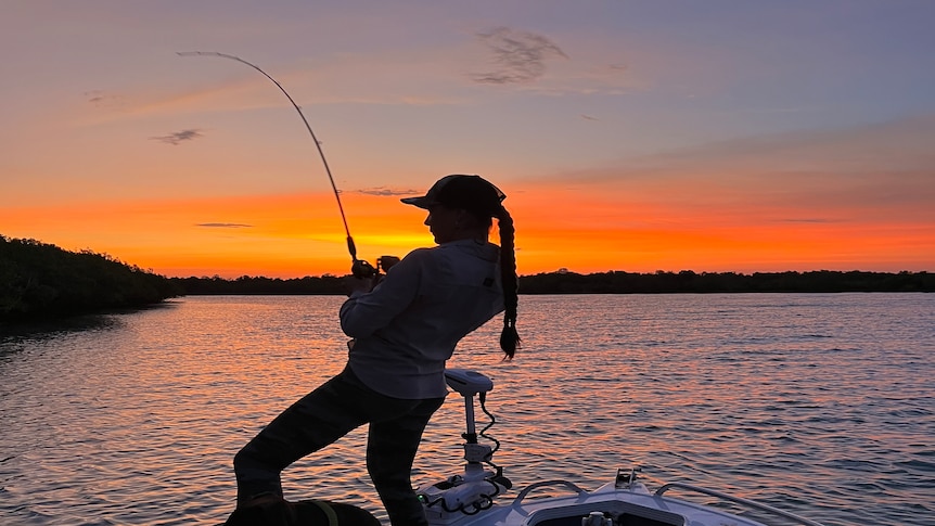 A woman, Loren Hanton, fishing off a boat during sunset