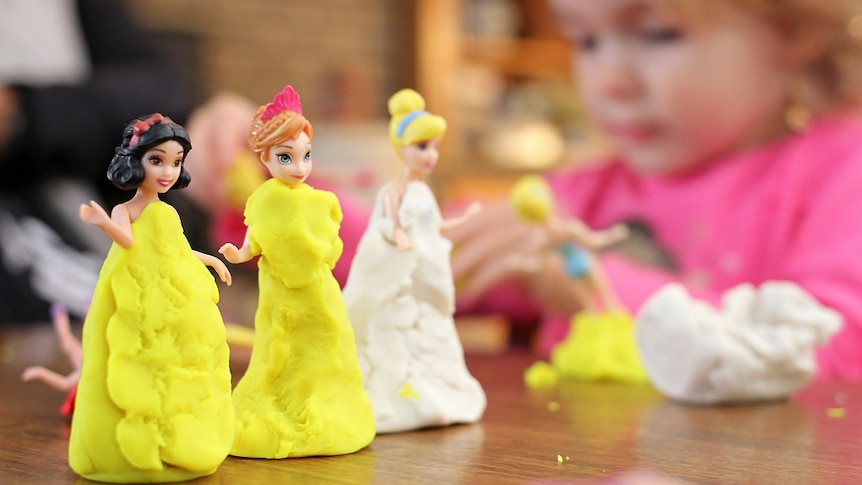 Three princess dolls wrapped in plasticine dresses as a girl plays, depicting traditional gender stereotypes for young girls.