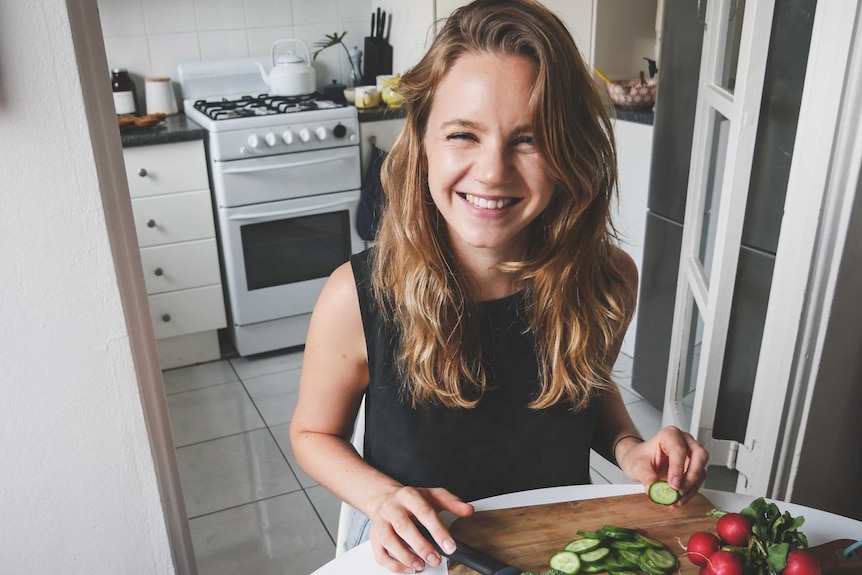 Nutritionist and caterer Kate Levins sitting at table and chopping vegetables, with a small kitchen in the background.