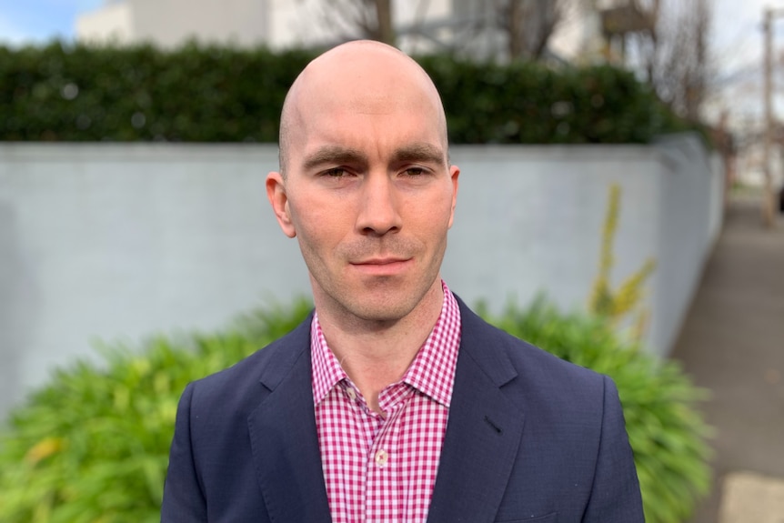 A bald man wearing a suit jacket and business shirt poses for a portrait.