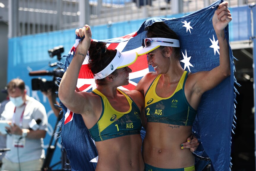 Two women wearing green and yellow bikinis hold a blue flag