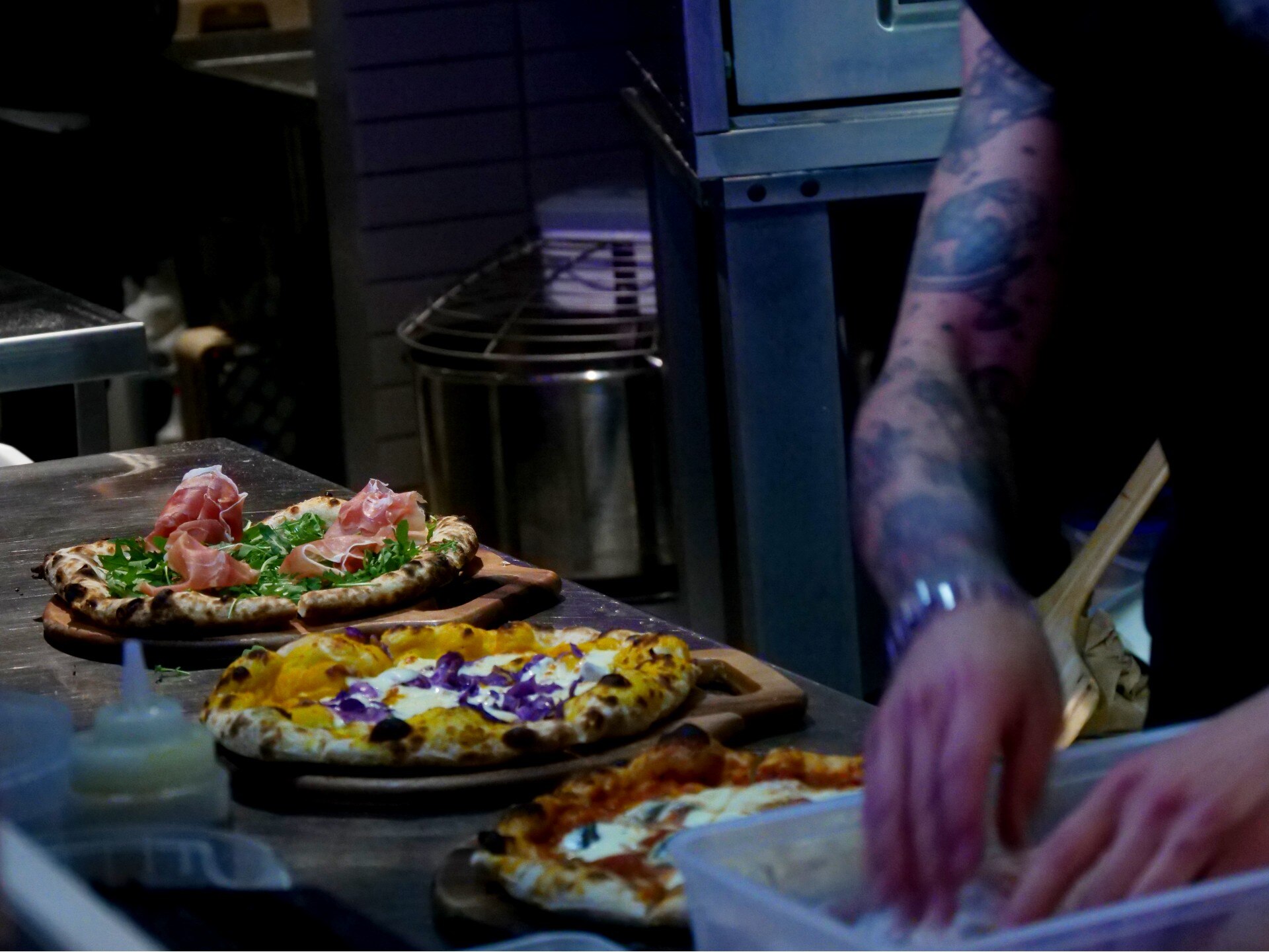 Three pizzas and the blurred hands of someone preparing them in a restaurant