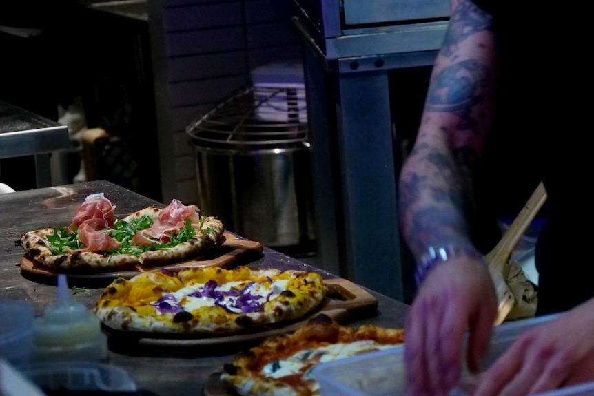 Three pizzas and the blurred hands of someone preparing them in a restaurant