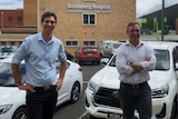 Two men wearing business shirts stand smiling towards the camera with the Bundaberg Hospital in the background.
