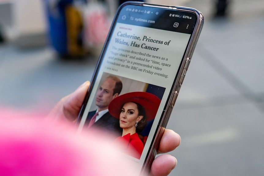 A hand holding a smartphone showing an article about Princess Catherine's cancer diagnosis. 