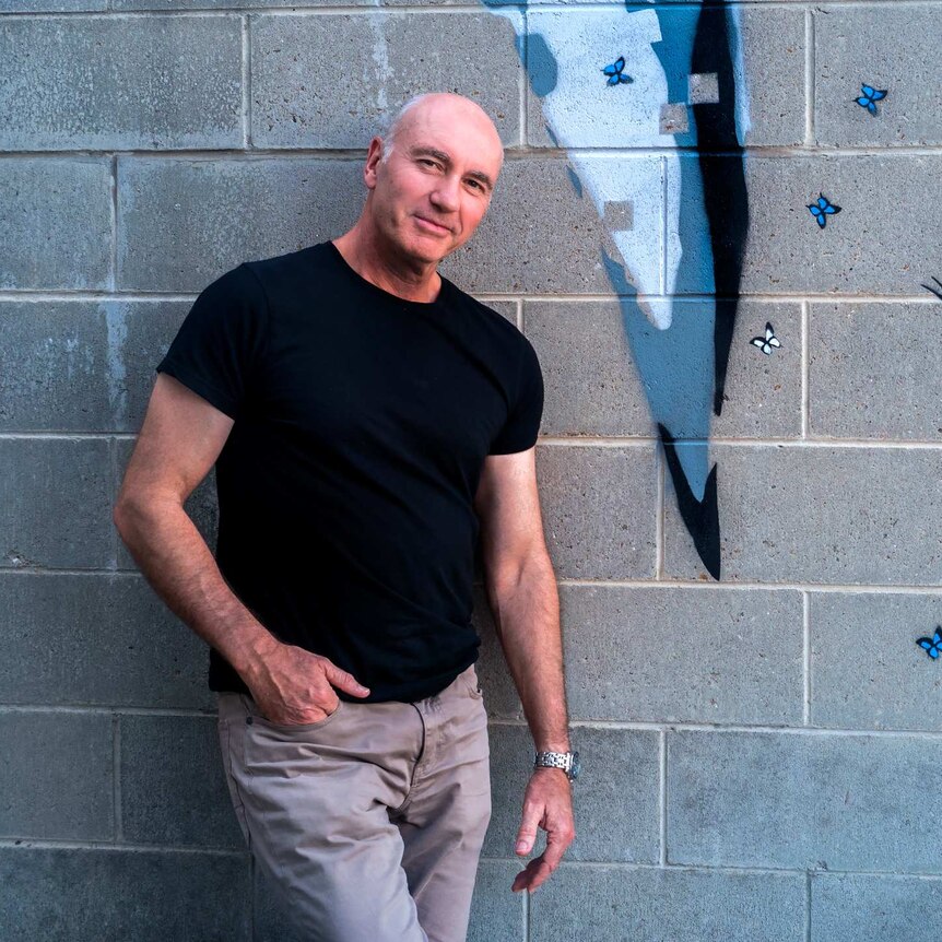 David Dowsett standing in front of street art spray painted on a brick wall.