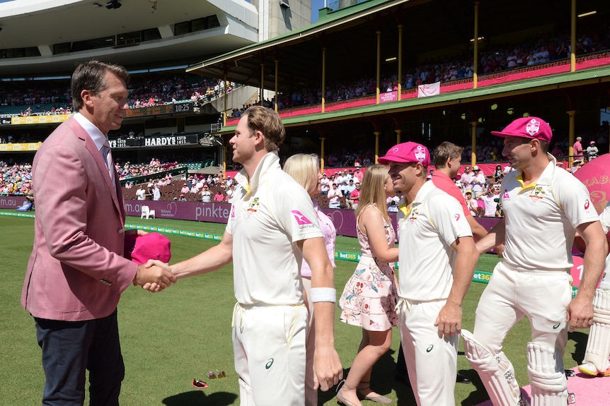 Three cricketers in baggy pink hats shake hands with Glenn McGrath wearing a suit