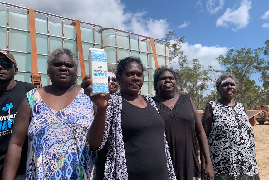 A middle-aged Aboriginal woman holds a carton of water, standing with other women in front of a truck.