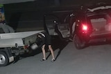 A still taken from security camera footage that shows a man in dark clothing tinkering with a ute.