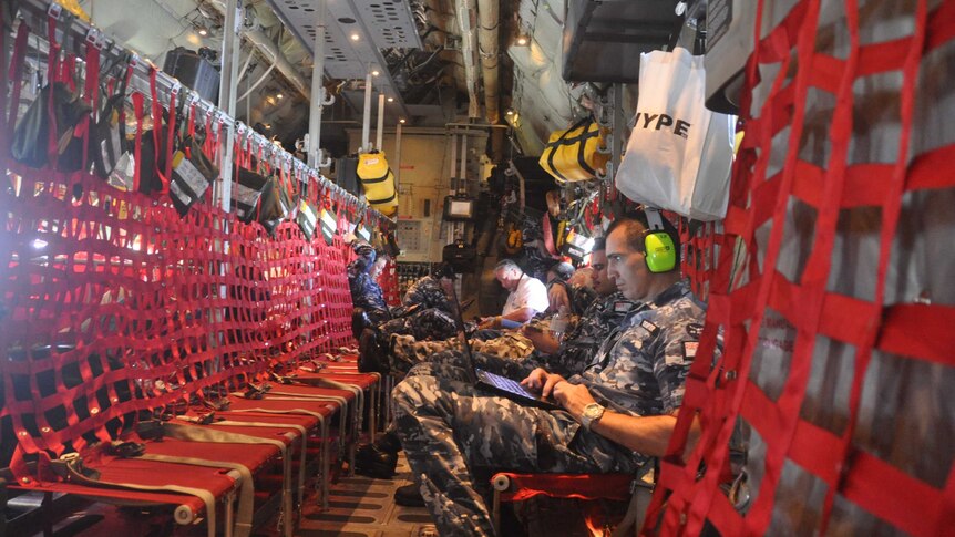 NASA scientists and members of the Australian Air Force tap away on keyboards aboard a Hercules jet.