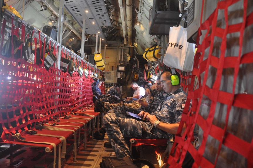 NASA scientists and members of the Australian Air Force tap away on keyboards aboard a Hercules jet.