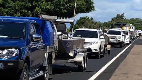 Four wheel drives towing boats on a straight stretch of road with traffic backed up.