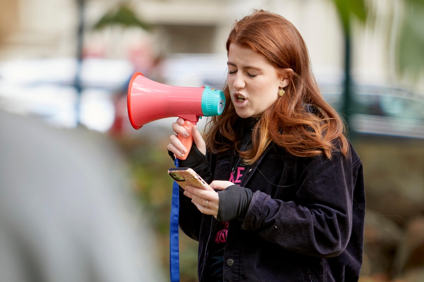 A young woman with red hair speaking into a megaphone.