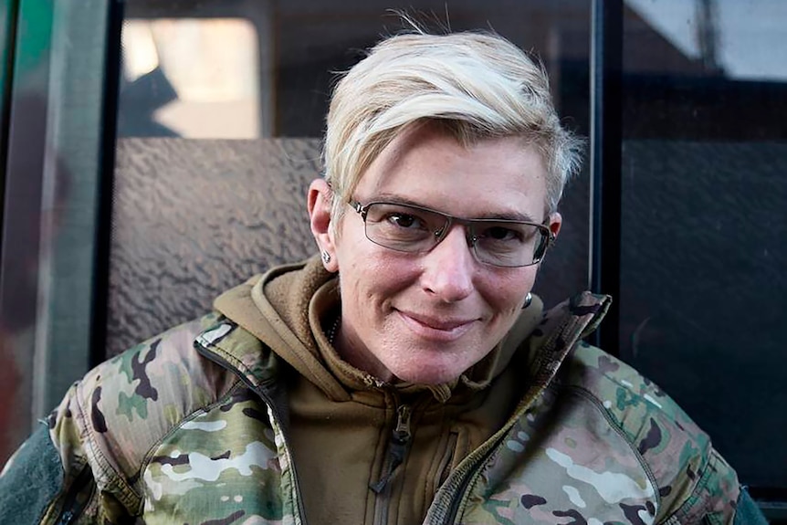 Блондинка в очках и военной форме улыбается для фото