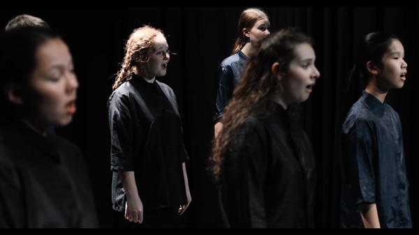5 teenagers are singing in a dark setting in navy tops.