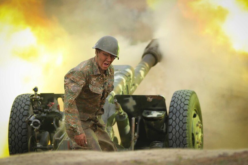 A man in camouflage grimaces as a artillery cannon fires.