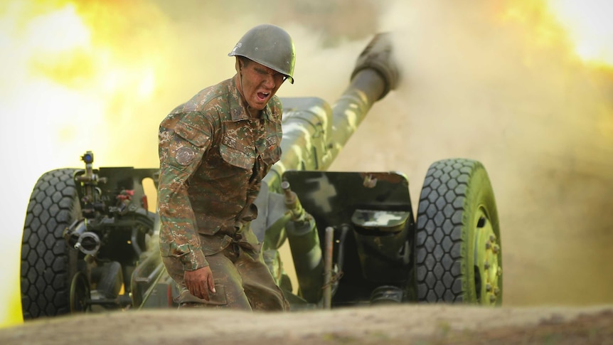 A man in camouflage grimaces as a artillery cannon fires.