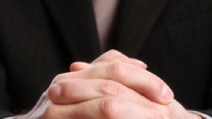 Close-up of praying hands on an open bible.