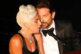 Lady Gaga and Bradley Cooper sing into a microphone seated next to each other