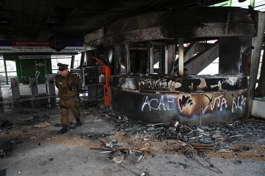 A police officer surveys the burnt out remains of a subway entrance.