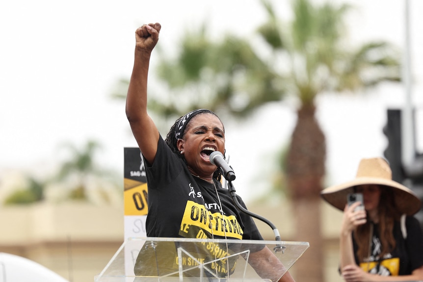 A Black woman stands at a podium with her fist in the air.