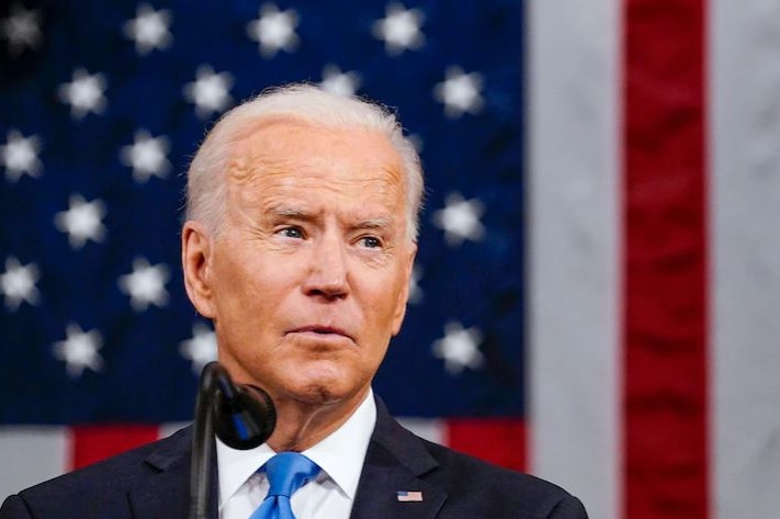Joe Biden speaking into a microphone in front of an American flag
