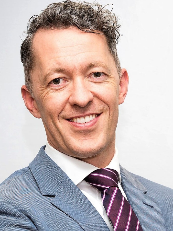 A man in a grey suit and burgundy tie folds his arms while smiling in a professional head shot