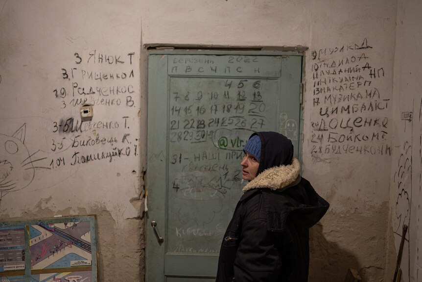 Halyna Tolochina stands in front of a wall inscribed with the names of people who died inside a school basement.