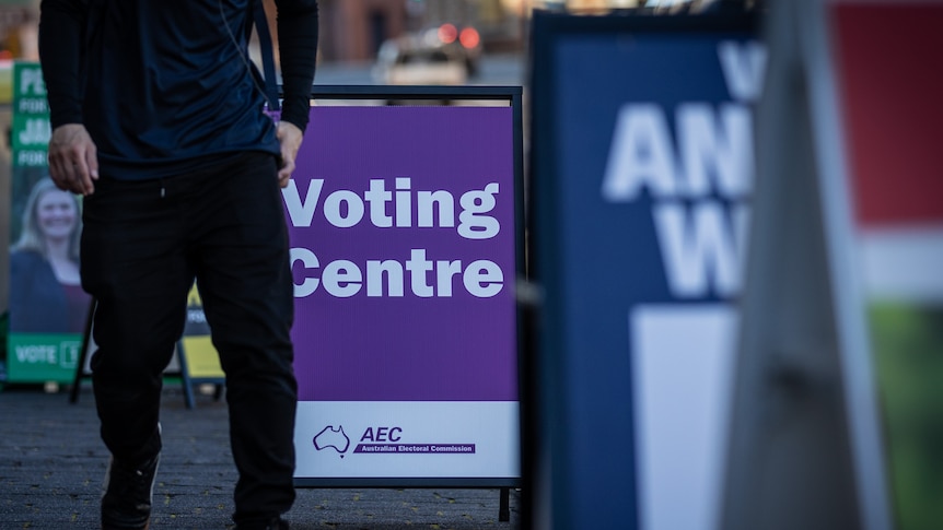 Unidentified person walks past a 'voting centre' sign in a street.