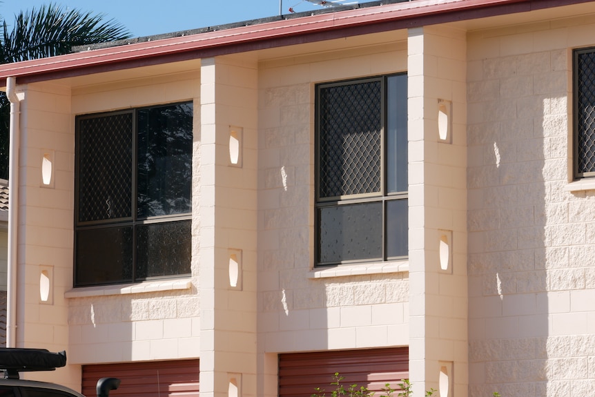 A tight shop of the windows on the second story of a brick house painted pink. 