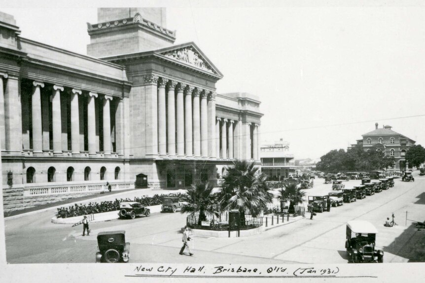 A black and white photo of the newly-opened Brisbane City Hall in 1931 with old black cars lined up in front of it.