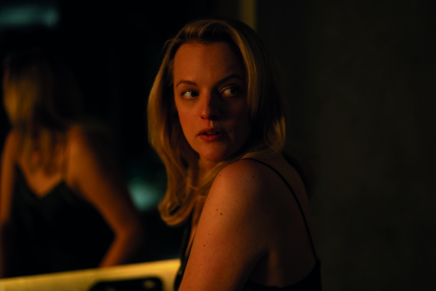 Elisabeth Moss looks over her shoulder in a darkened room
