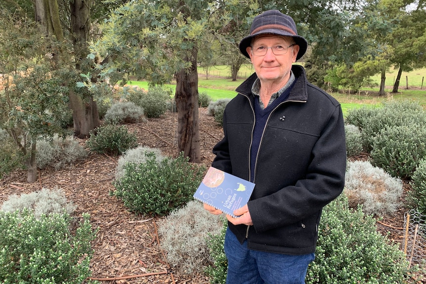 A man with a hat holds a pamphlet in a nice garden.