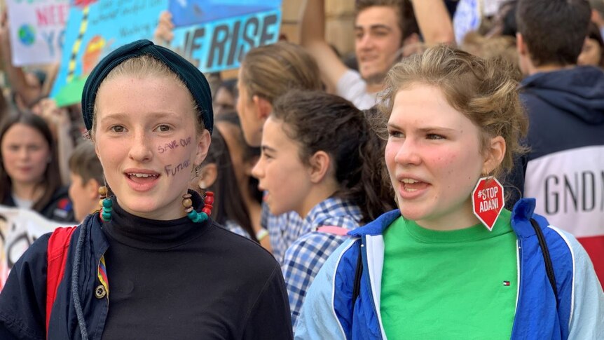 Two girls, standing in a scrum of other students, many holding signs.