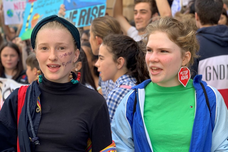 Two girls, standing in a scrum of other students, many holding signs.