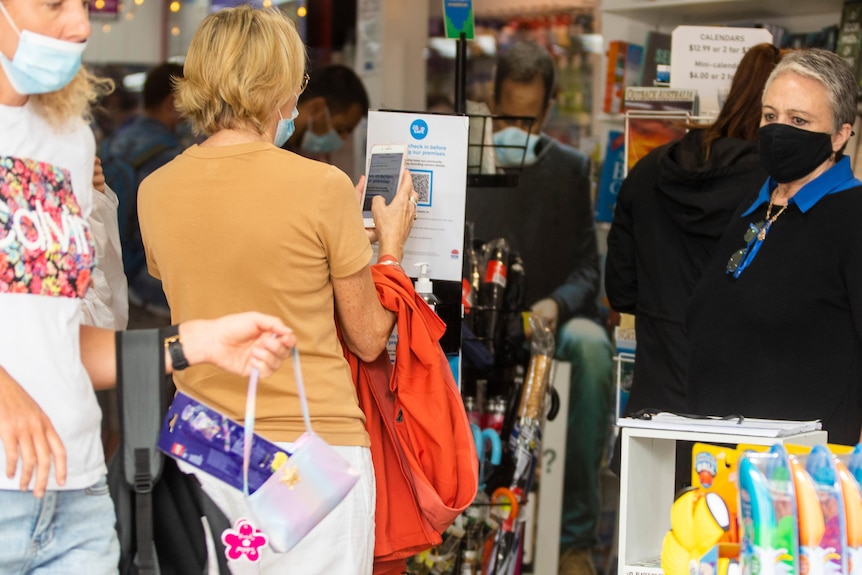 A woman uses a QR code to enter a shop while an employee looks on
