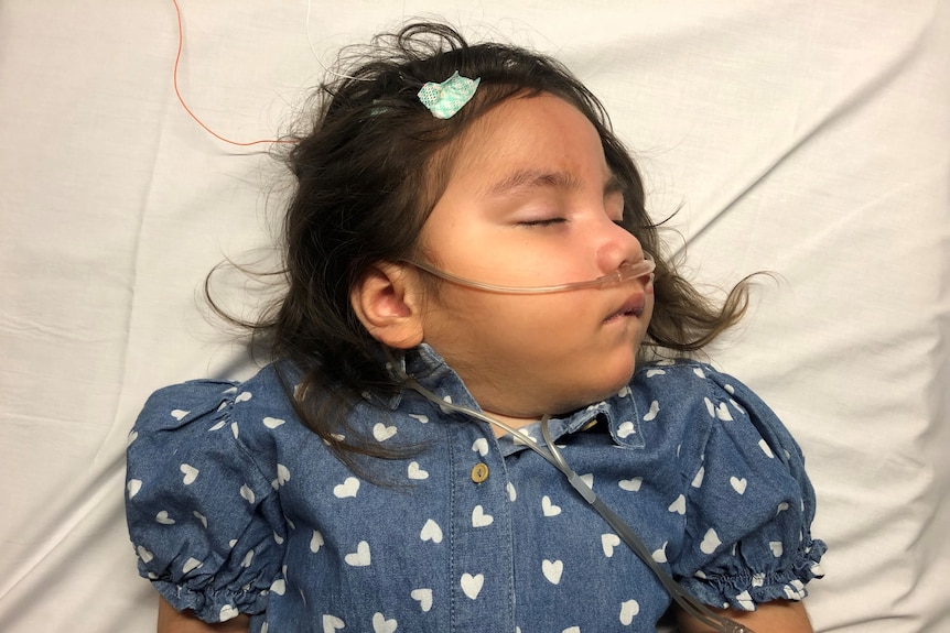 Jasira wears a blue dress as she rests on a hospital bed