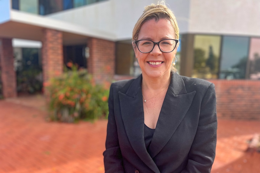 Lady wearing black jacket and black glasses stands in front of building in Carnarvon