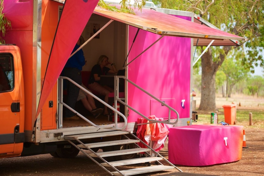 The door on the side of a bright pink Telstra van is open, with a remote park in the background.