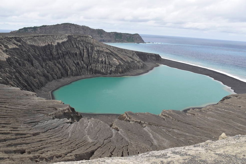 A wide shot shows the cliffs and black sand of a small island.