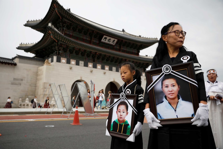 A child and a woman hold portraits of another child and woman with a confusius temple in the background.