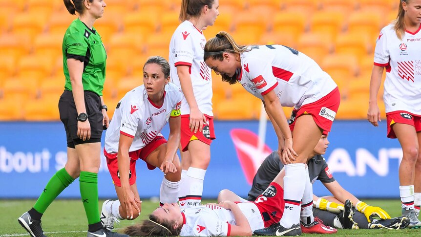 A woman lies on the floor, surrounded by her Adelaide United team mates
