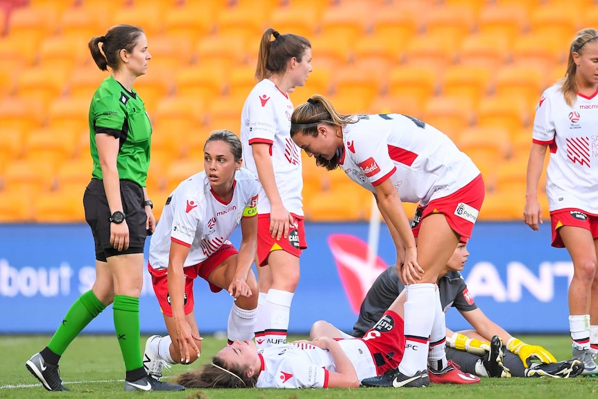 A woman lies on the floor, surrounded by her Adelaide United team mates