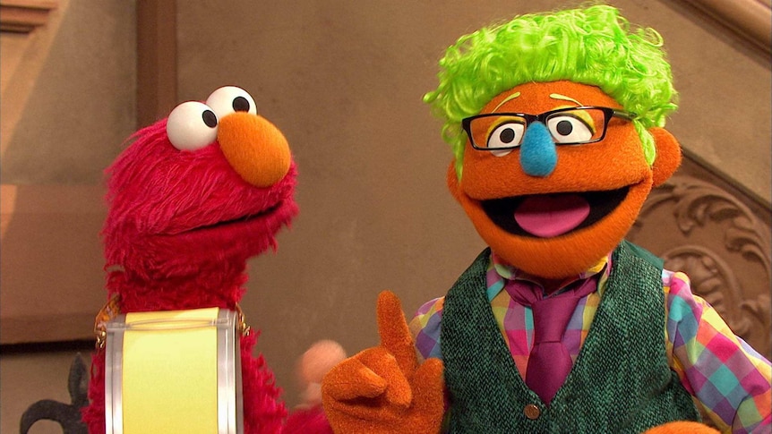 Elmo, holding a drum, with Buzz Word who is sticking up his index finger