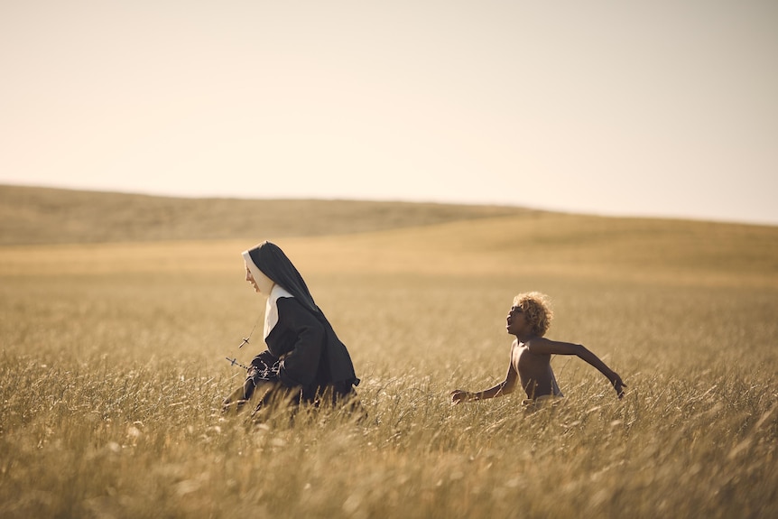 Cate Blanchett, a middle-aged white woman in a nun's habit, and Aswan Reid, a young Aboriginal boy, run through a wheat field.