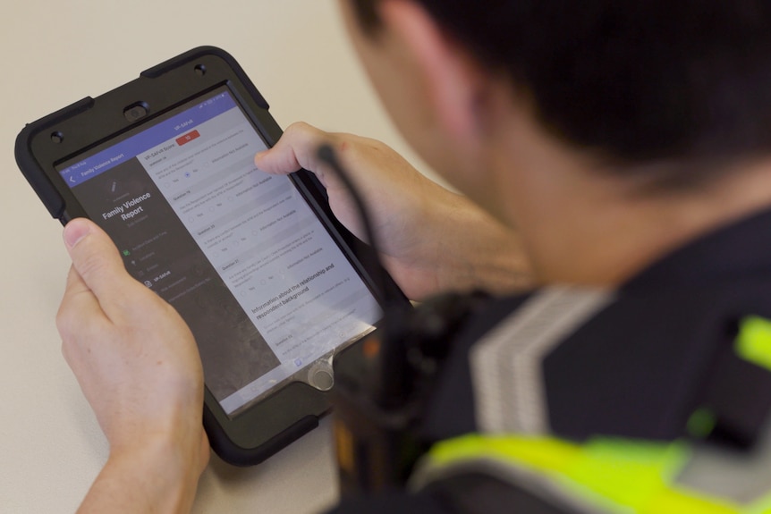 A Victoria Police officer with dark hair holds an iPad